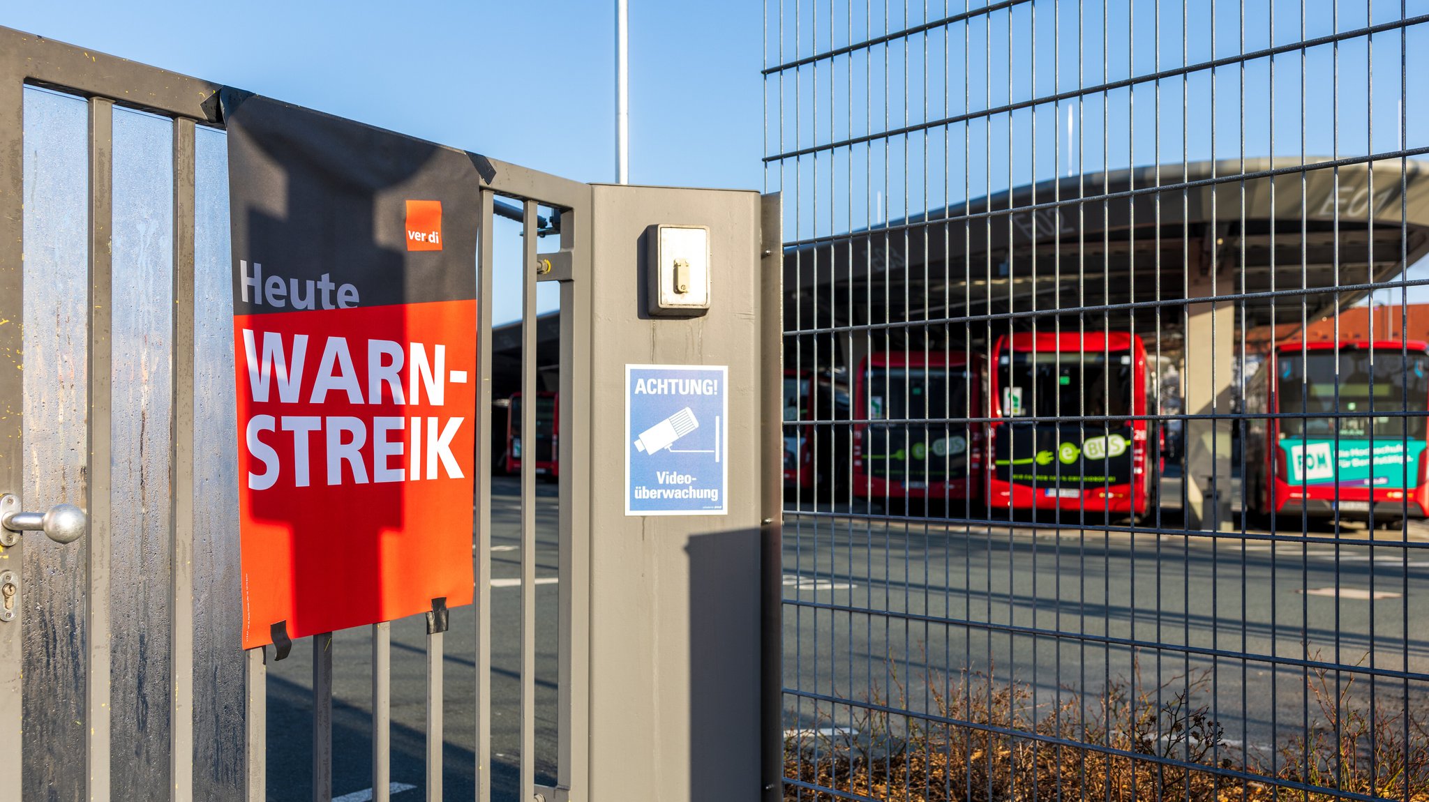 (Archivbild) Ein Hinweisschild der Gewerkschaft Verdi mit der Aufschrift "Heute Warnstreik" ist am Eingangstor des VAG-Betriebshofs Schweinau angebracht. Im Hintergrund stehen mehrere Linienbusse auf dem Gelände und kommen aufgrund des Warnstreiks im öffentlichen Nahverkehr nicht zum Einsatz.