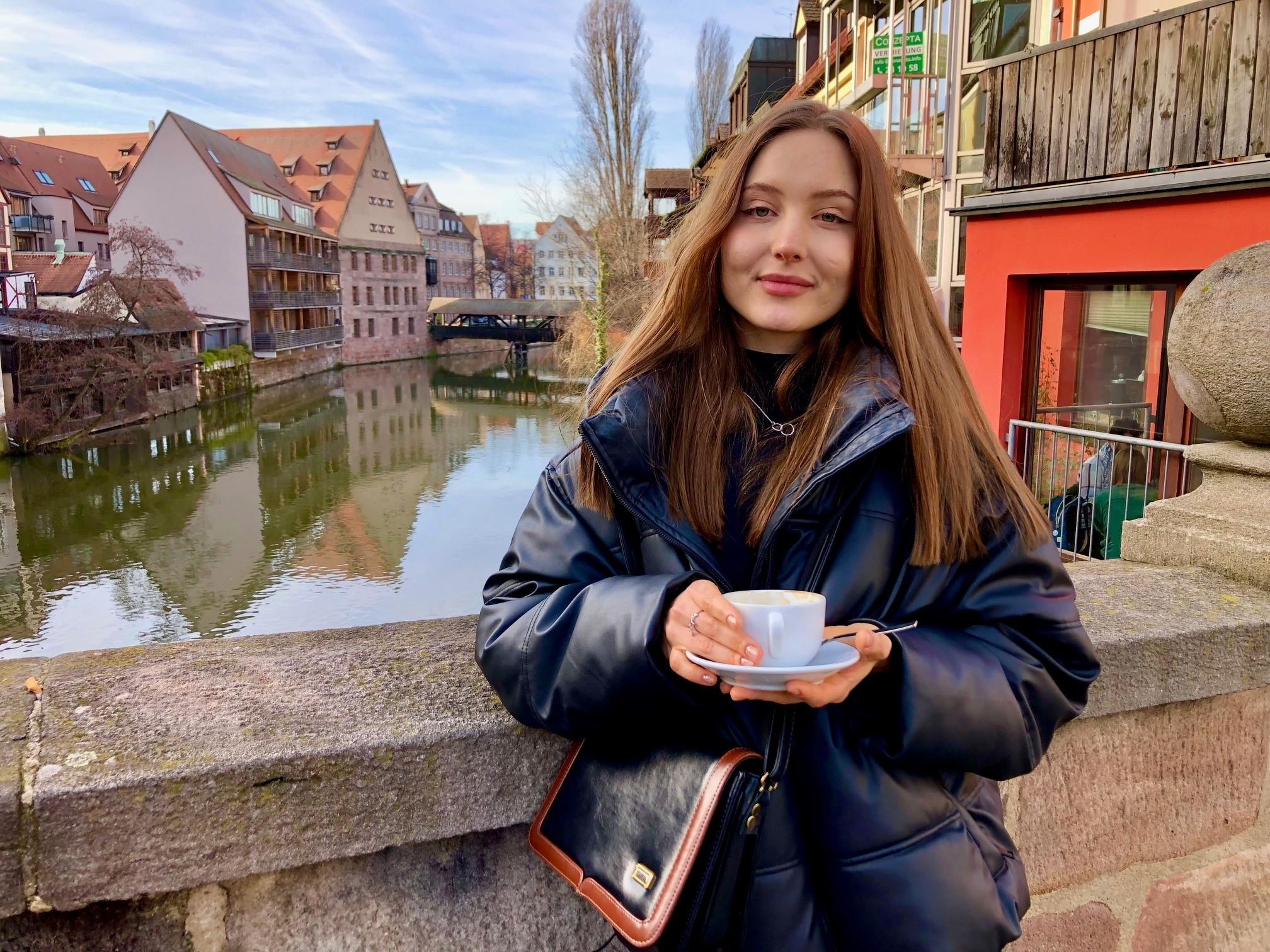 Junge Frau mit einer Tasse Kaffee auf einer Brücke in der Nürnberger Altstadt.