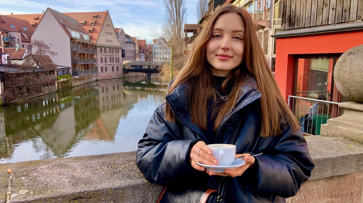 Junge Frau mit einer Tasse Kaffee auf einer Brücke in der Nürnberger Altstadt.
