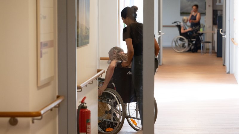 Eine Pflegerin schiebt einen Patienten im Rollstuhl. | Bild: picture alliance / SvenSimon | Malte Ossowski / SVEN SIMON Eine Pflegerin schiebt einen Patienten im Rollstuhl.