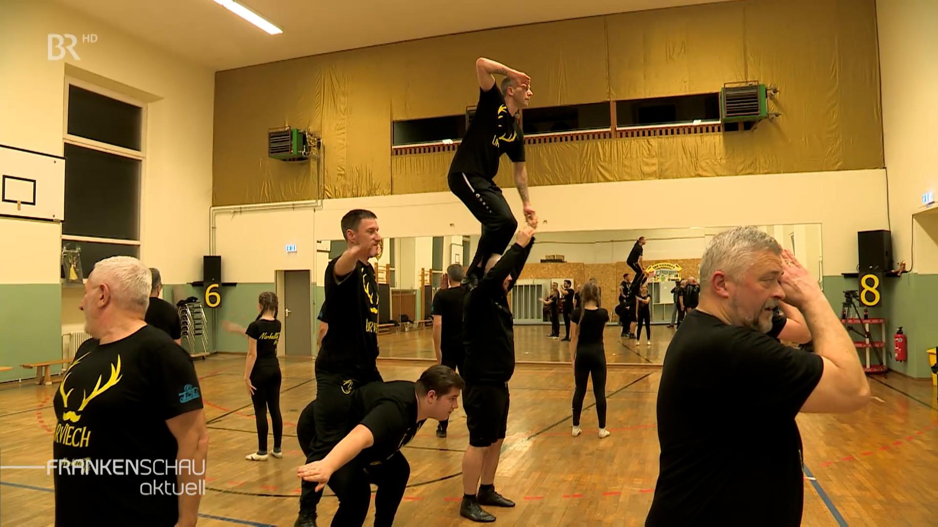 Männer in schwarzen Trikots trainieren in einer Turnhalle. 