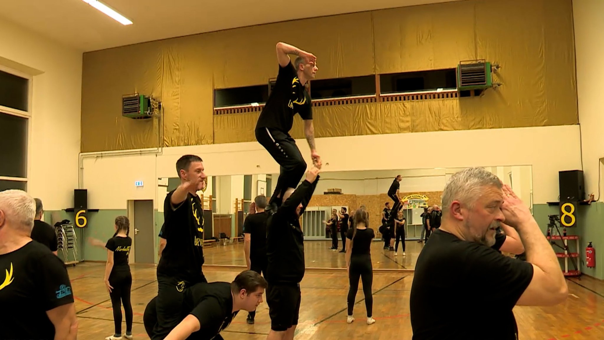 Männer in schwarzen Trikots trainieren in einer Turnhalle. 