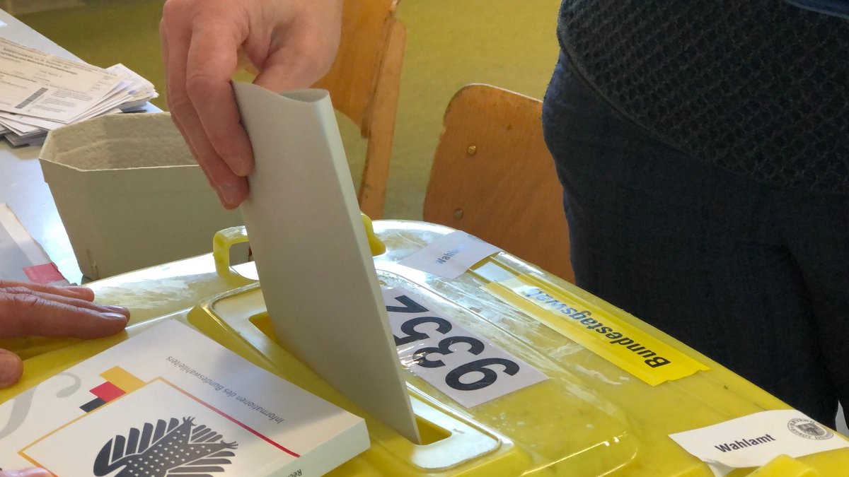 Jemand steckt einen Wahlzettel in eine knallgelbe Wahlurne