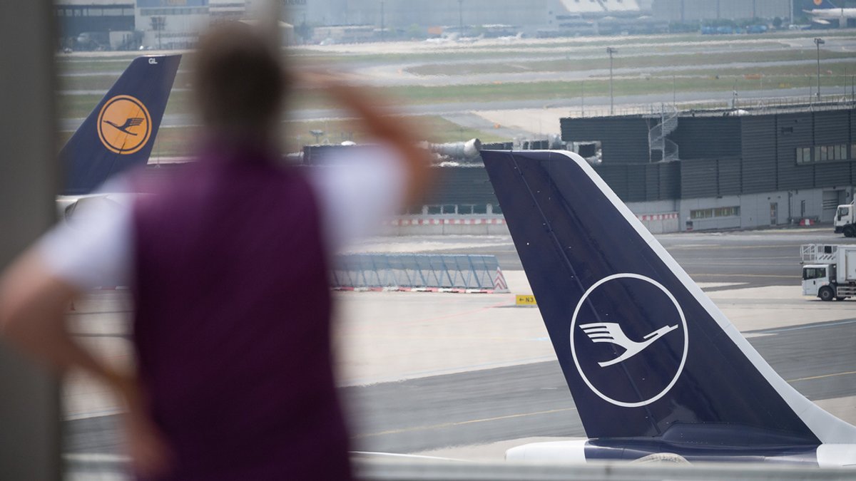 Eine Frau schaut am Flughafen Frankfurt in Richtung eines Flugzeugs mit dem Logo der Lufthansa auf der Heckflosse.