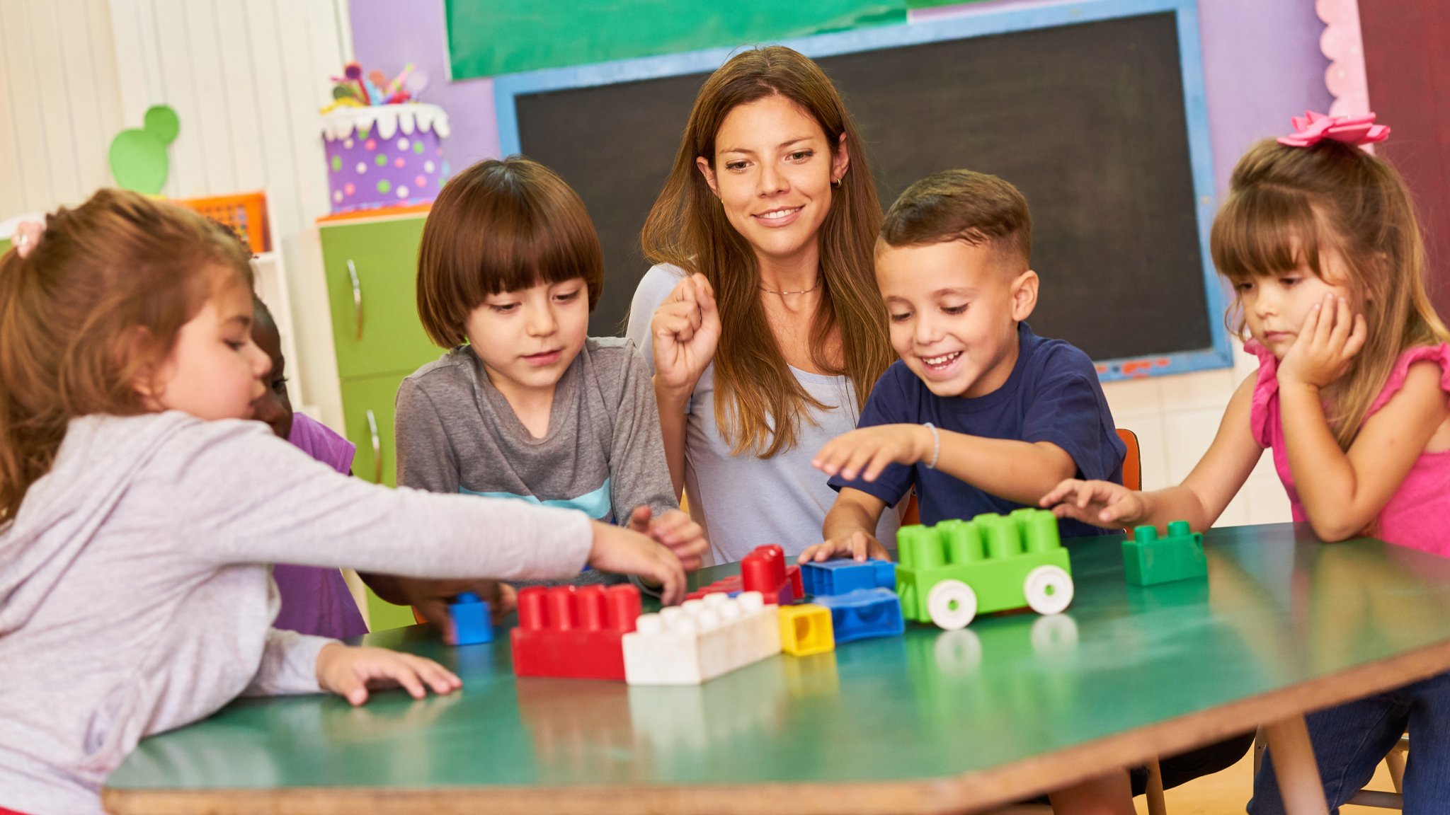 Kindergarten-Kinder spielen zusammen mit einer Erzieherin mit Bausteinen