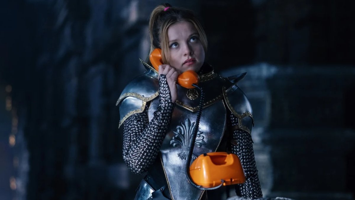 Junge Frau in Ritterrüstung telefoniert mit einem analogen Telefon 