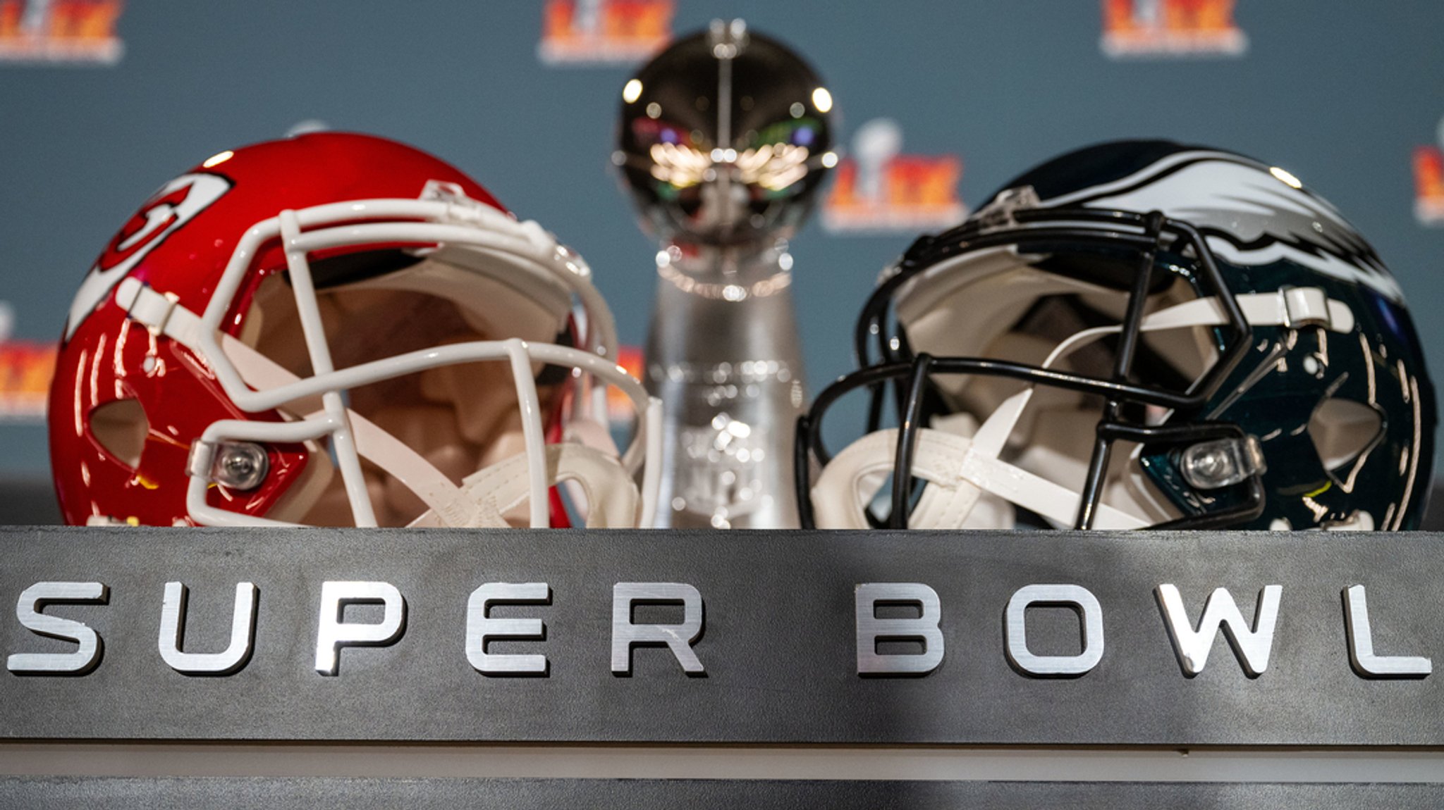 Die Vince Lombardy Trophy und die beiden Helme der teilnehmenden Mannschaften, Kansas City Chiefs und Philadelphia Eagles, stehen auf einem Podest vor einer Pressekonferenz.