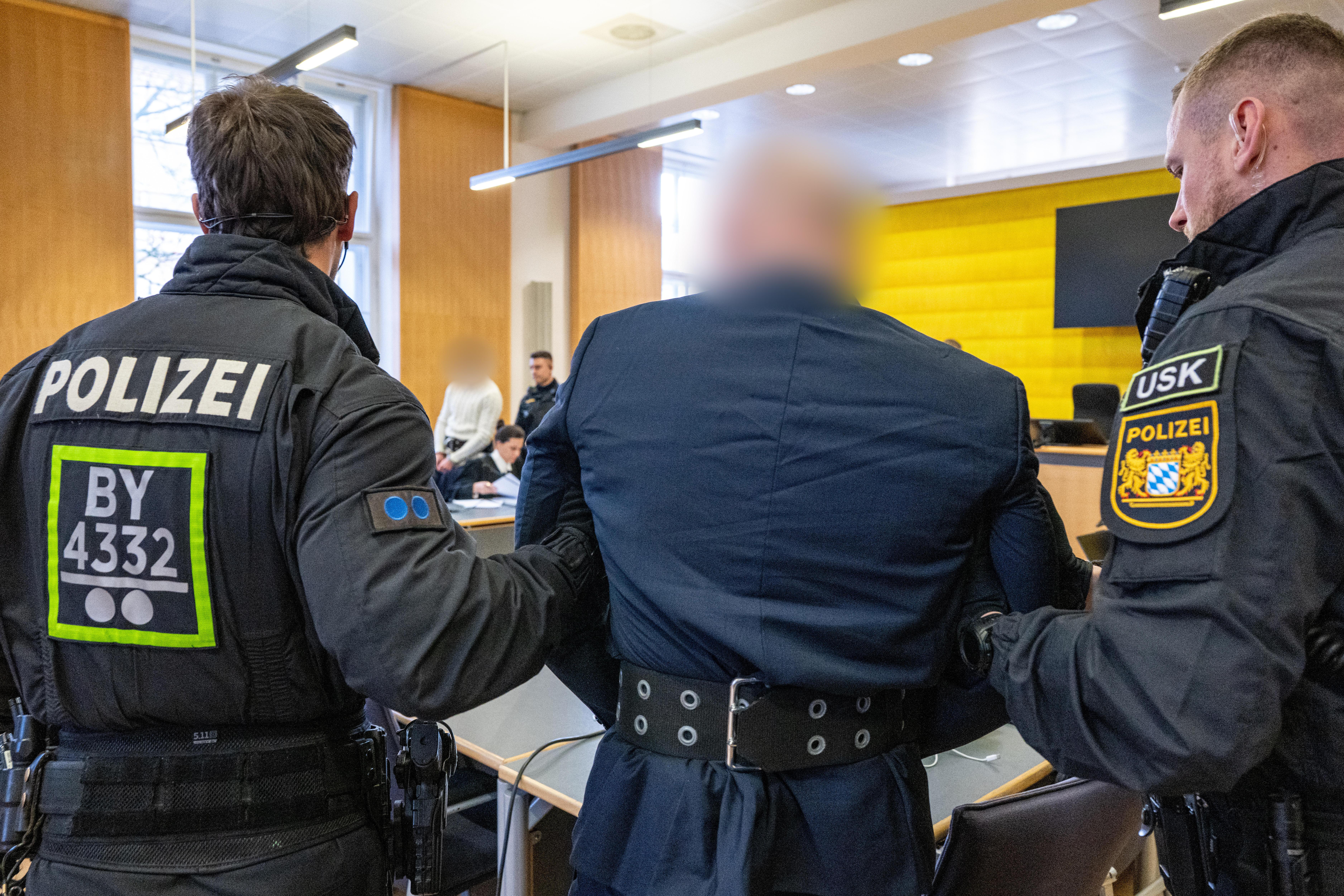 Die angeklagten Männer, die im August 2024 aus dem BKH in Straubing geflohen waren, werden von Polizisten in den Verhandlungssaal des Landgerichts Regensburg geführt. 