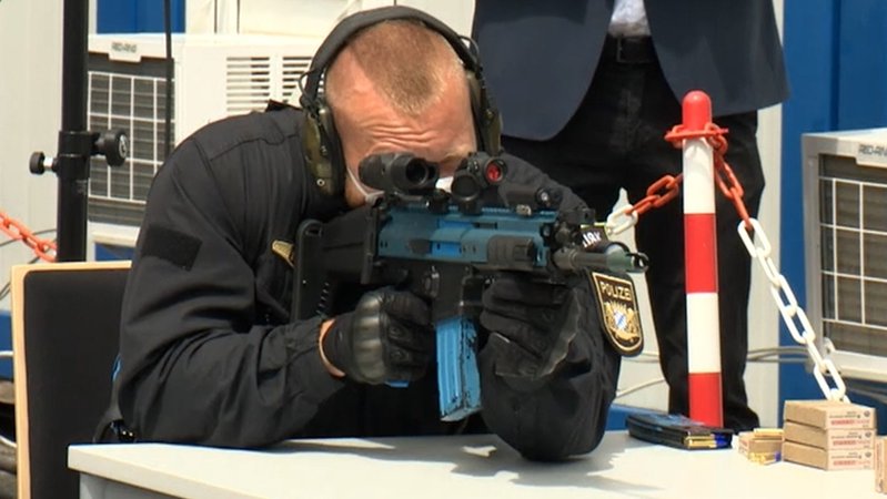 Ein Polizist in Uniform stützt sich auf einem Tisch auf und schießt mit einer Laser-Maschinenpistole