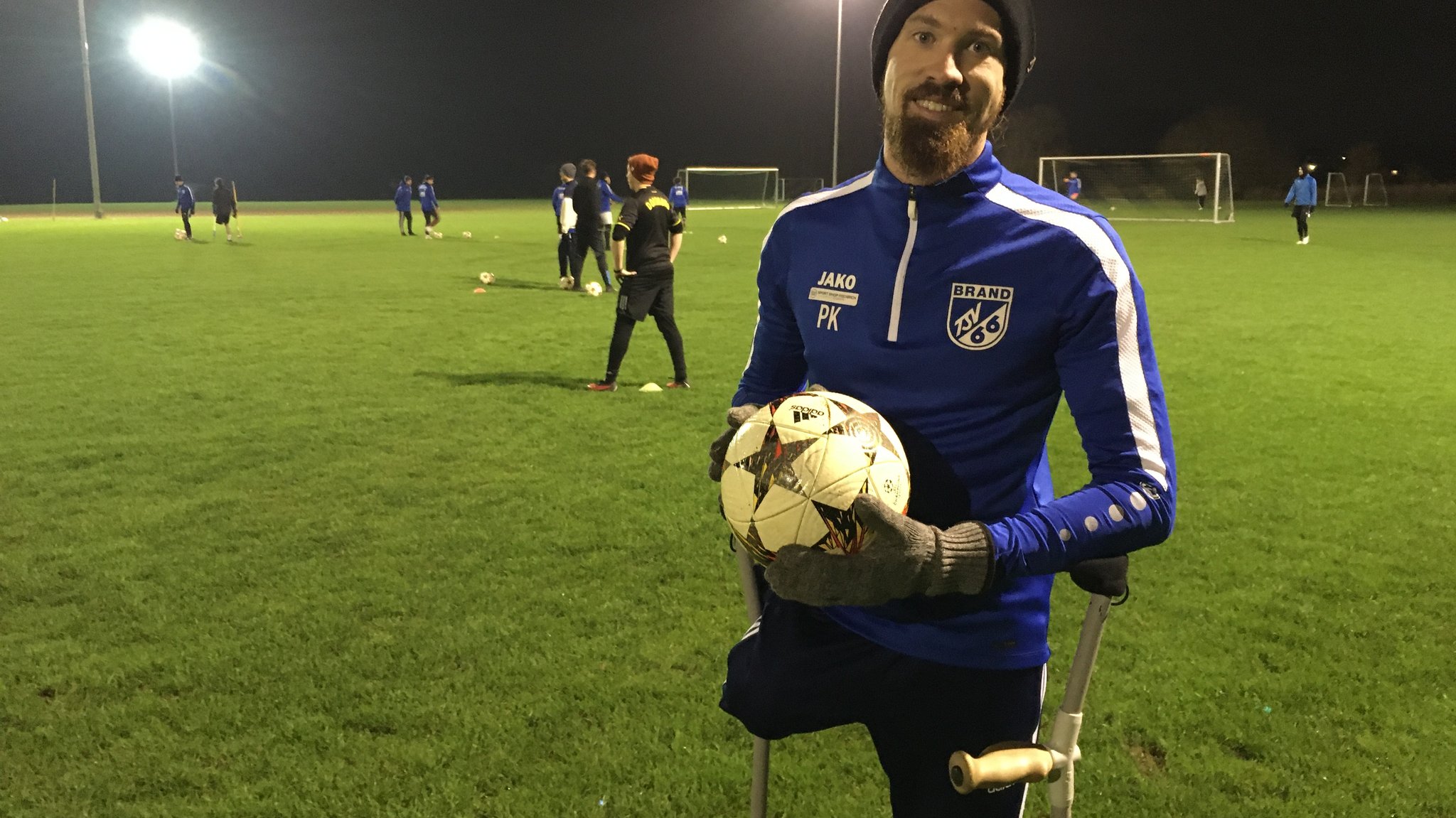 Pierre Kaiser steht an Krücken mit einem Fußball in der Hand auf einem Fußballplatz.