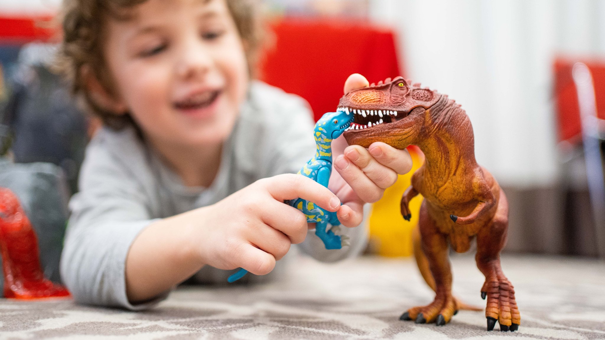 Zu sehen ist ein Junge, der mit zwei Schleich-Dinosauriern spielt 