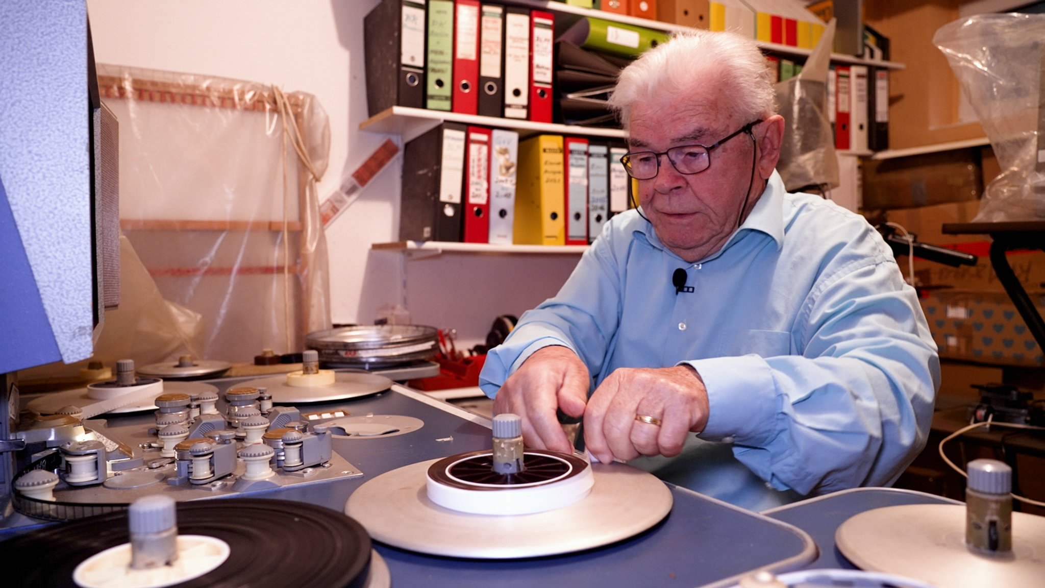Werner Flott sitzt konzentriert an großen Filmrollen an seinem alten Schnitttisch.