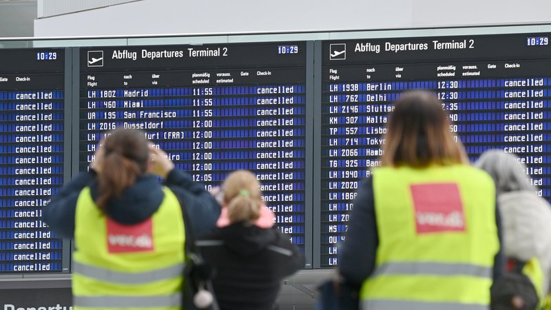 Streikende am Münchner Flughafen vor den Anzeigetafeln, die die ausgefallenen Flüge anzeigen.