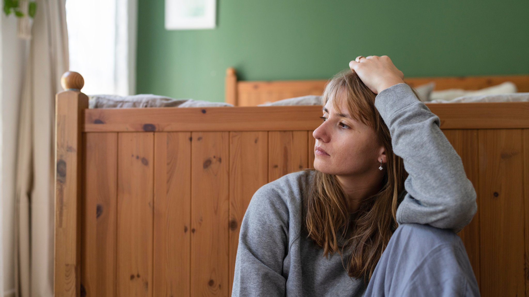 Symbolbild: Nachdenkliche Frau hockt neben einem Bett, die Hand in den Haaren