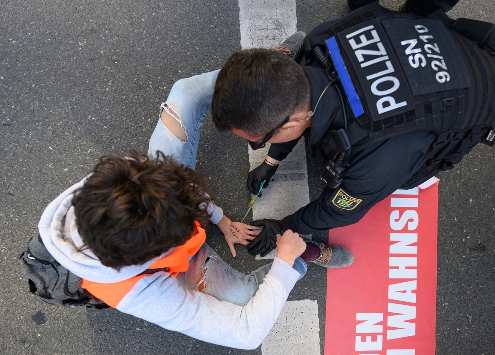 16.05.2022, Sachsen, Dresden: Umweltaktivisten der Gruppe «Letzte Generation» haben sich auf der Fahrbahn fest geklebt und ein Polizist versucht den Kleber zu lösen. Die Protestler fordern auf weitere fossile Energie zu verzichten. 
