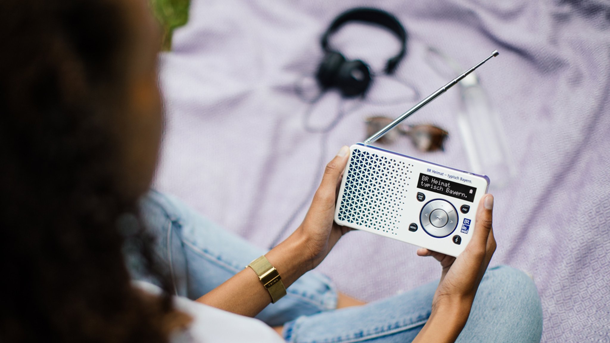SYMBOLBILD Eine Frau sitzt mit einem DAB+ - Radio auf einer Picknickdecke.