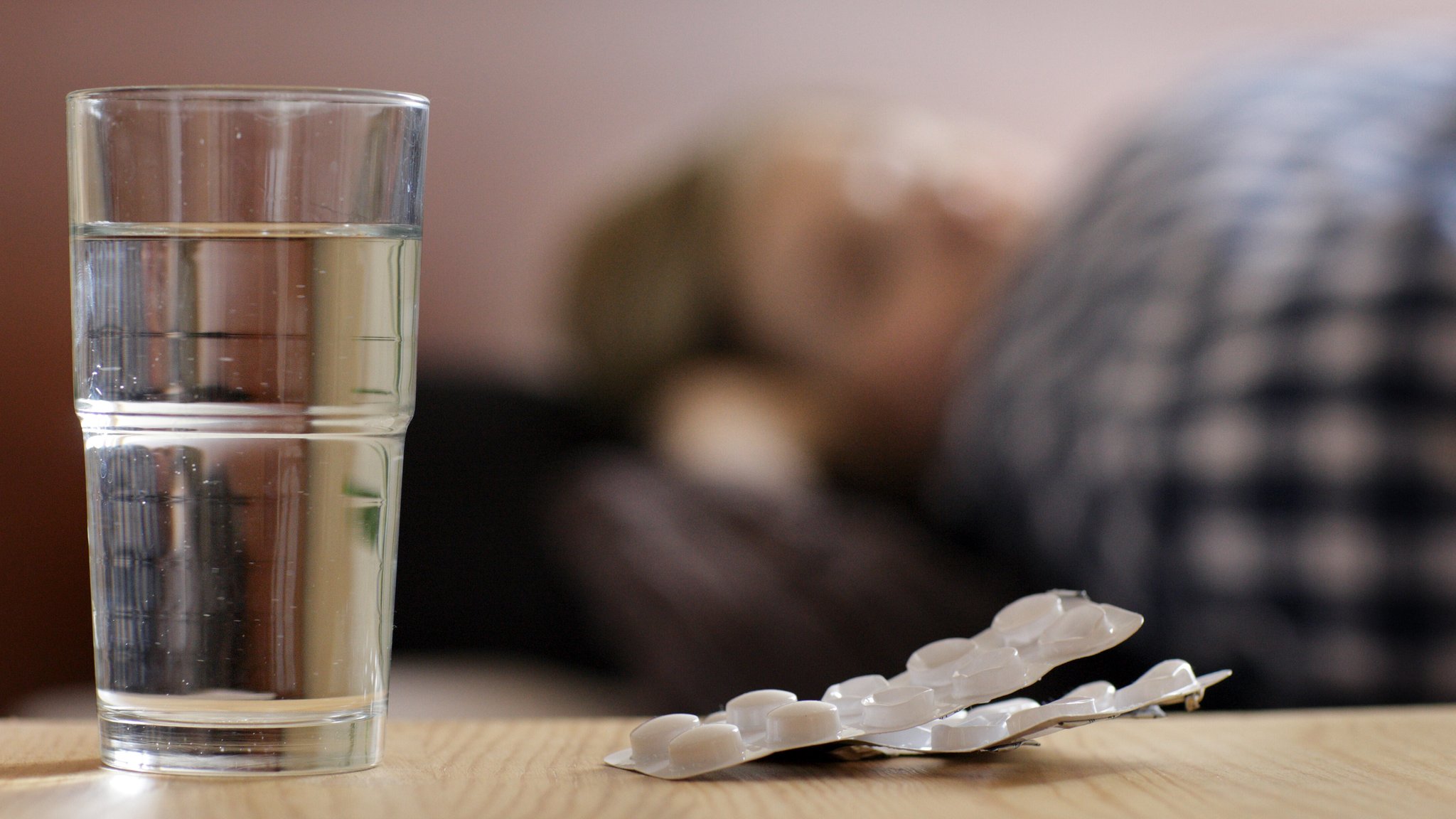 (Symbolbild) Ein Wasserglas, daneben ein Tablettenblister. Im Hintergrund liegt eine Person im Bett. | Bild: picture alliance / photothek | Ute Grabowsky (Symbolbild) Ein Wasserglas, daneben ein Tablettenblister. Im Hintergrund liegt eine Person im Bett.