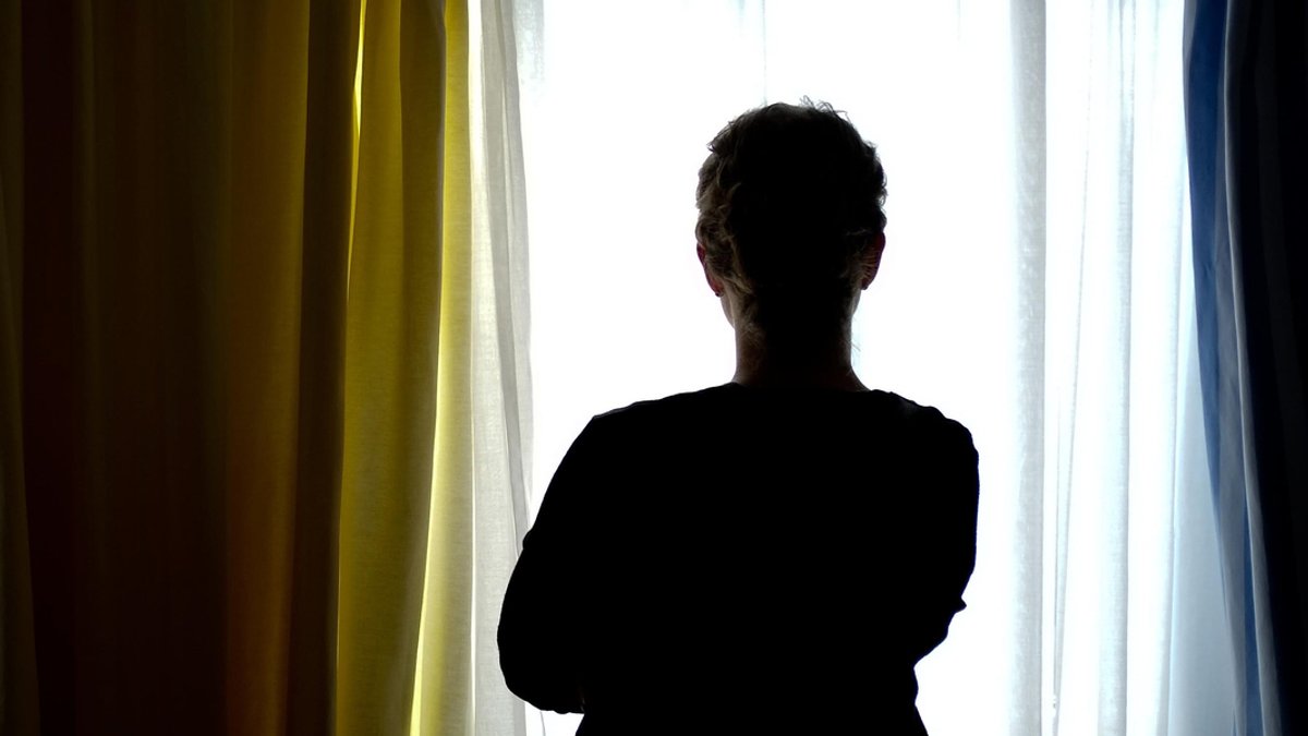 Eine Frau, die Opfer einer Gewalttat geworden ist, blickt aus dem Fenster.
