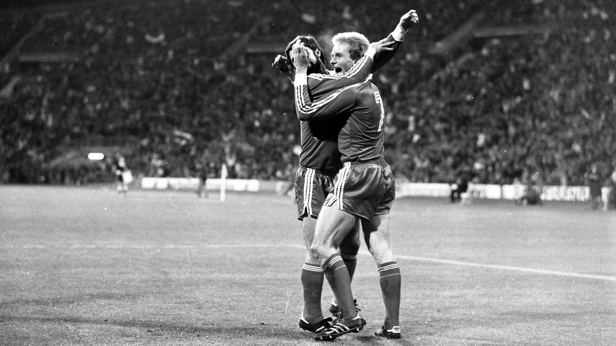 Schwarz-weißes Foto von Gerd Müller (l.) und Karl-Heinz Rummenigge, wie sie auf dem Fußballfeld jubeln und sich umarmen. 