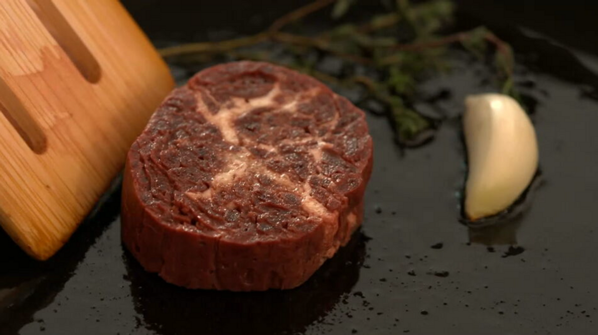 Auf einer heißen, fettigen Oberfläche wird ein Stück Fleisch aus Zellkultur angebraten.