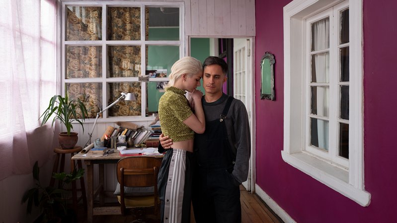 Ein Paar steht eng beieinander in einem Raum mit großem Fenster und violetter Wand, im Hintergrund ein Schreibtisch (Filmszene aus "Ema")