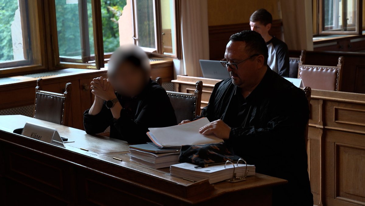 Eine Frau mit verpixeltem Gesicht sitz neben ihrem Anwalt im Gerichtssaal. 
