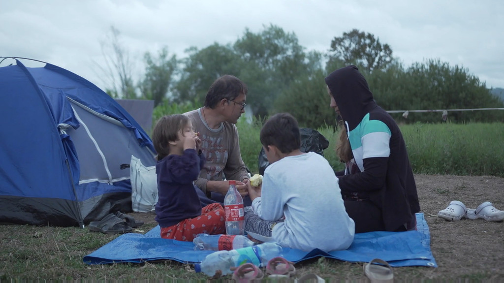 Hassan Gholam sitzt mit seiner Familie auf einer Decke und isst gemeinsam vor einem Zelt.