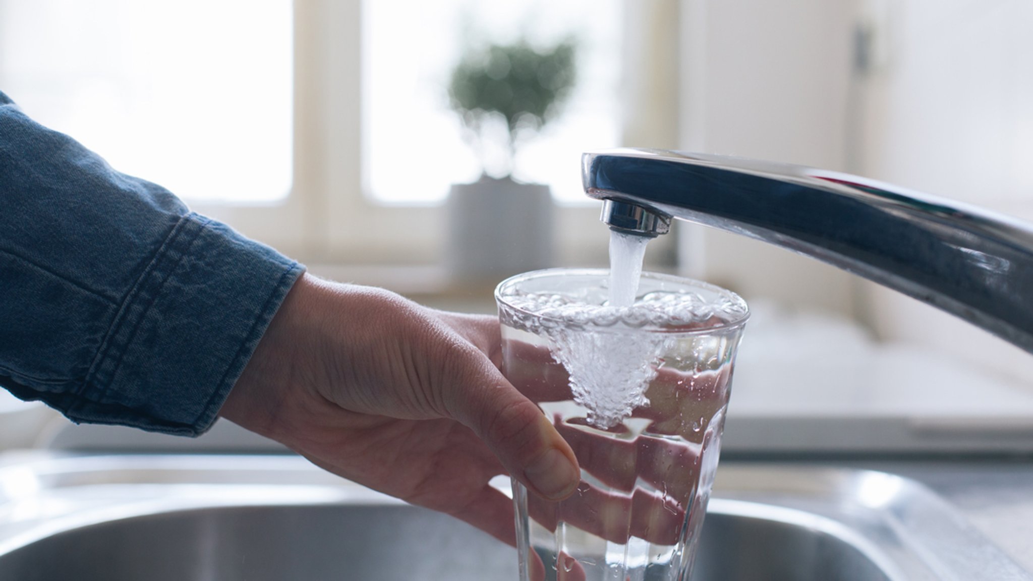 Jemand füllt am Wasserhahn ein Glas mit Leitungswasser.