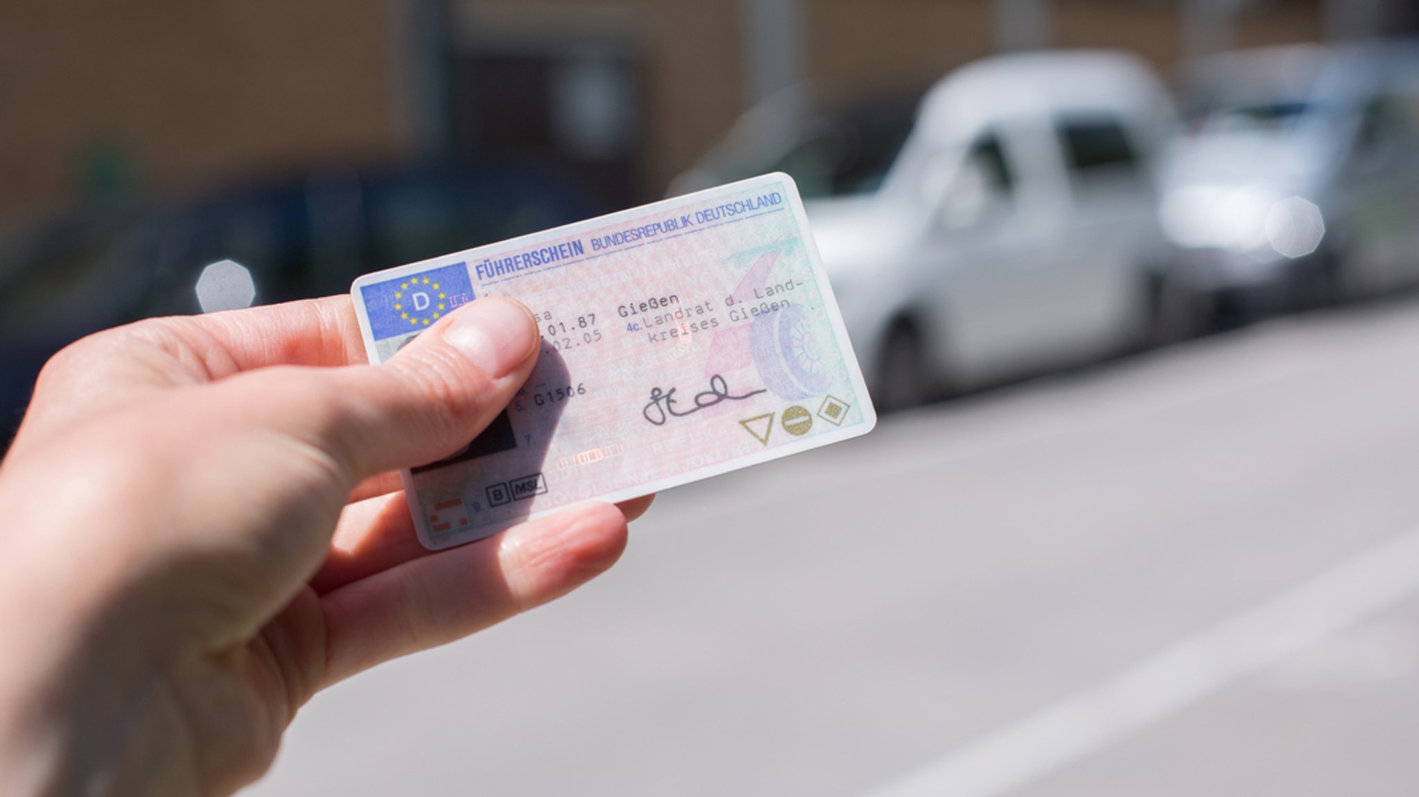 Jemand hält einen deutschen Führerschein vor mehreren Autos hoch.