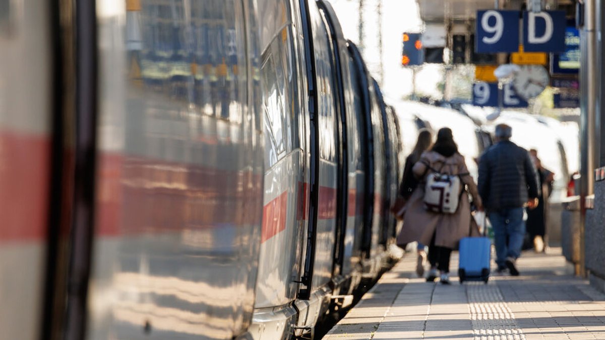 Reisende gehen mit Gepäck am Bahnsteig am Nürnberger Hauptbahnhof neben einem ICE entlang.