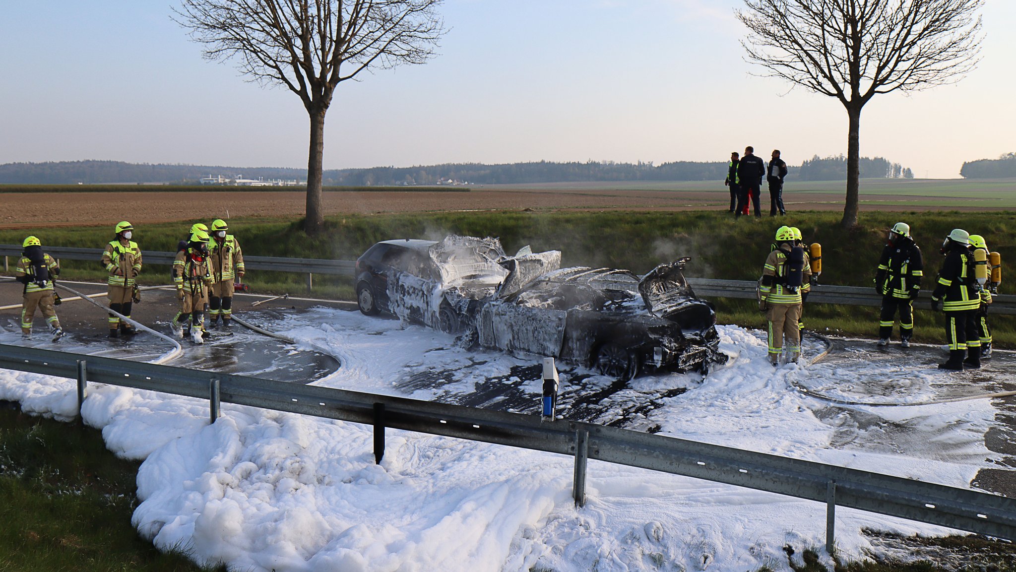 Die beiden Unfallautos stehen zwischen Feuerwehrleuten, die Straße ist voller Löschschaum