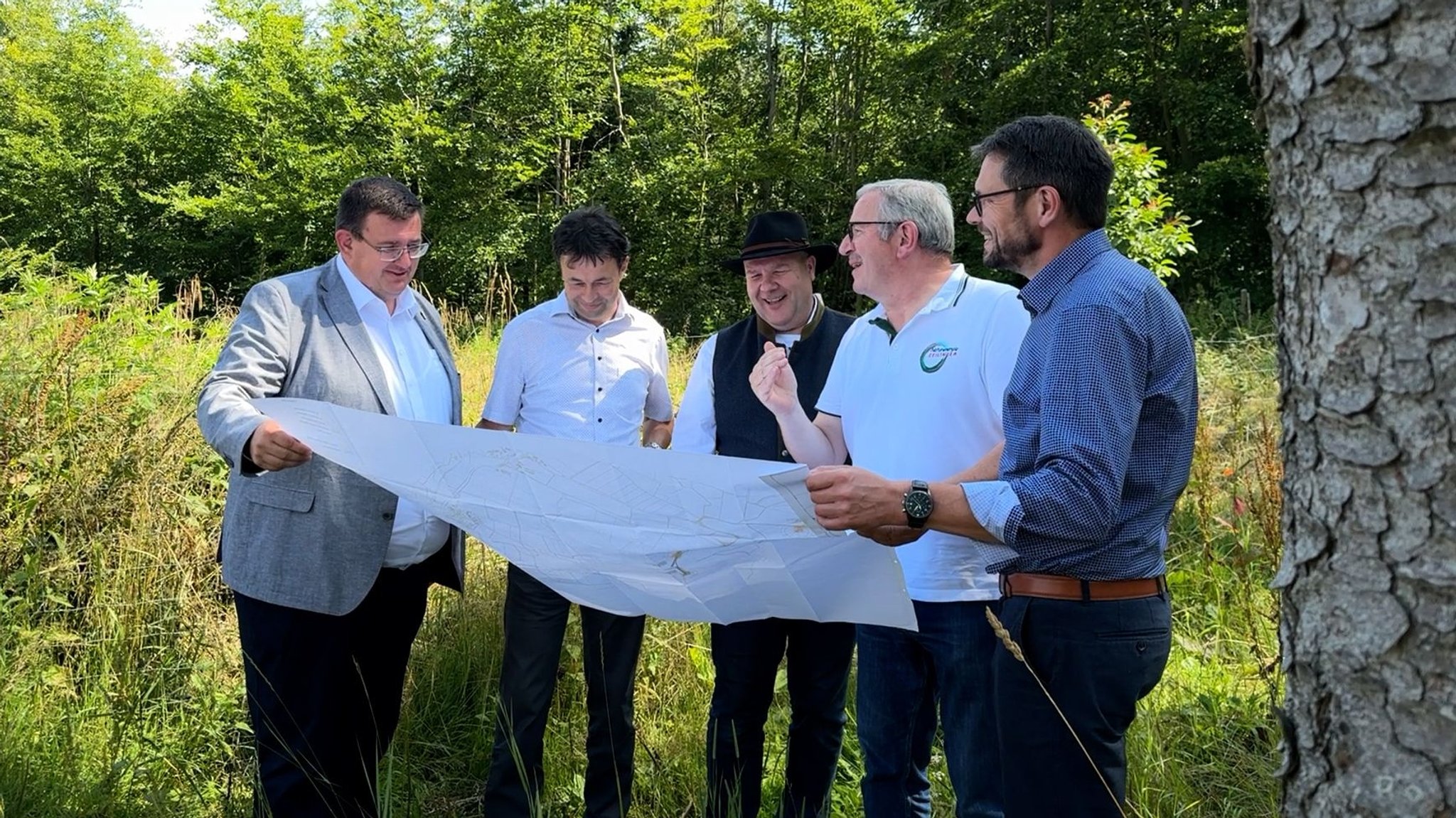 Fünf Männer stehen mit einer großen Landkarte im Wald.