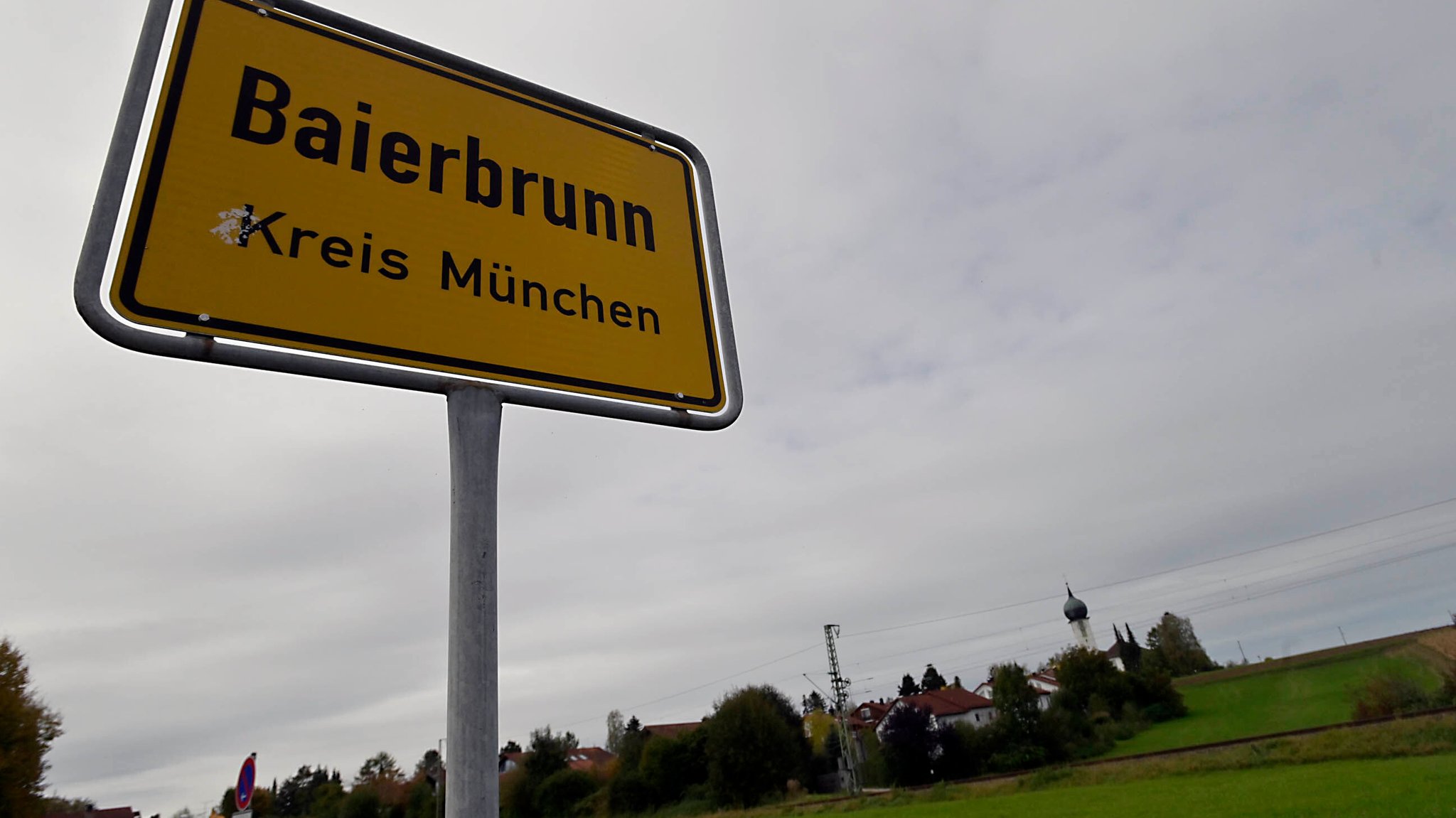 Ortschild von Baierbrunn. Im Hintergrund der Ort und die Kirche. | Bild: picture alliance / SZ Photo | Claus Schunk Ortschild von Baierbrunn. Im Hintergrund der Ort und die Kirche.
