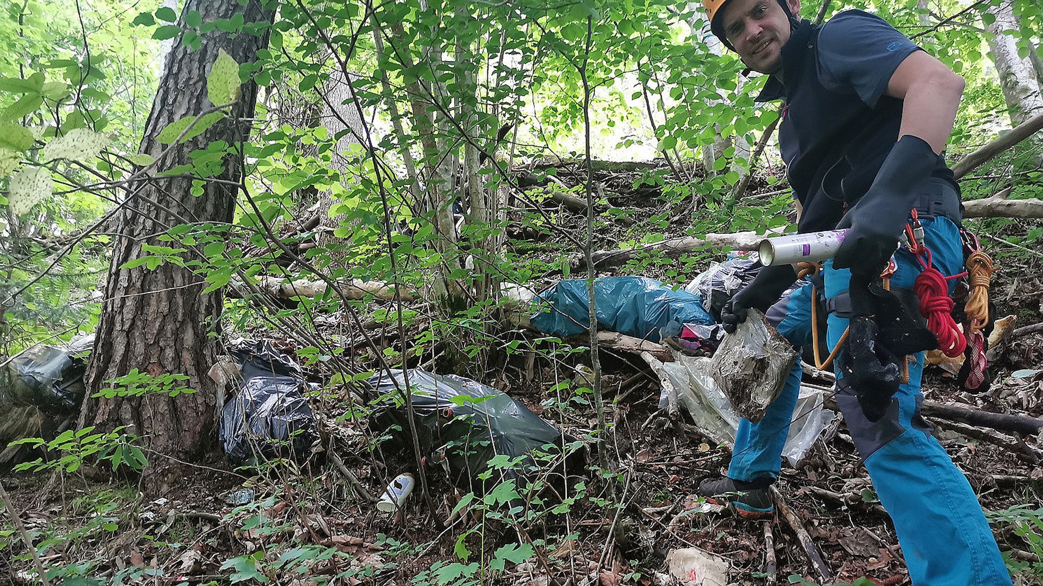 Ein Freiwilliger der Bergwacht sammelt mit Klettergurt Müllsäcke am Berghang.