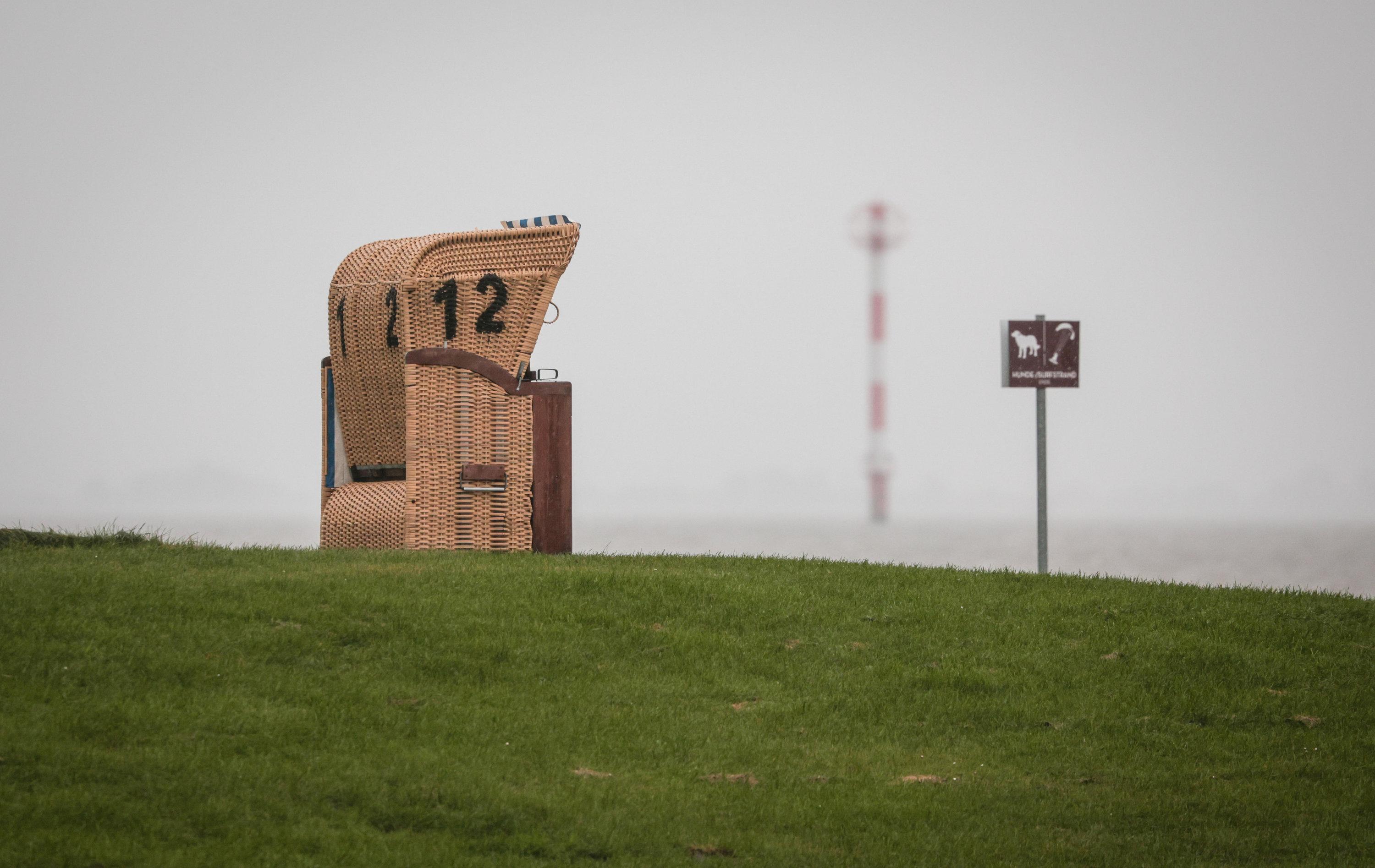 Ein leerer Strandkorb steht unter einem grauen, regnerischen Himmel am Kutterhafen von Wremen in Niedersachsen.