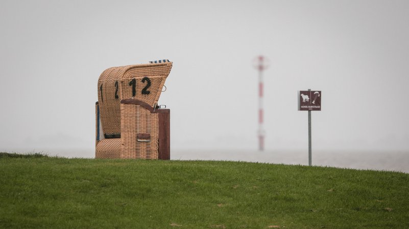 Ein leerer Strandkorb steht unter einem grauen, regnerischen Himmel am Kutterhafen von Wremen in Niedersachsen. | Bild: dpa-Bildfunk/Focke Strangmann Ein leerer Strandkorb steht unter einem grauen, regnerischen Himmel am Kutterhafen von Wremen in Niedersachsen.