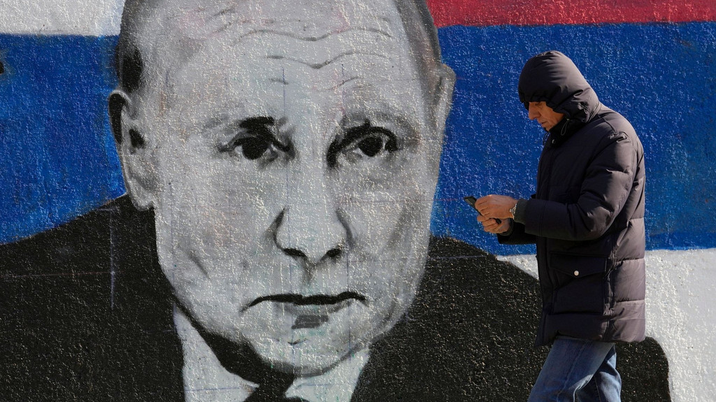 Eine Mann geht an einem Wandgemälde mit Putin vorbei.