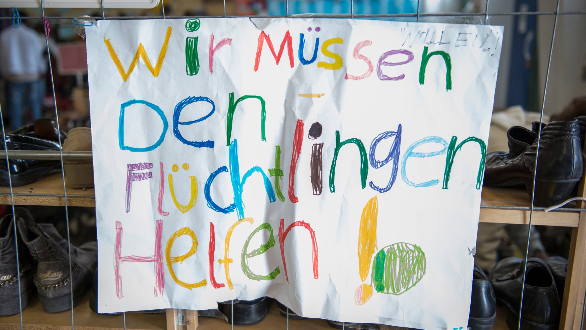 Ein buntes Plakat mit der Aufschrift: "Wir müssen den Flüchtlingen helfen!"