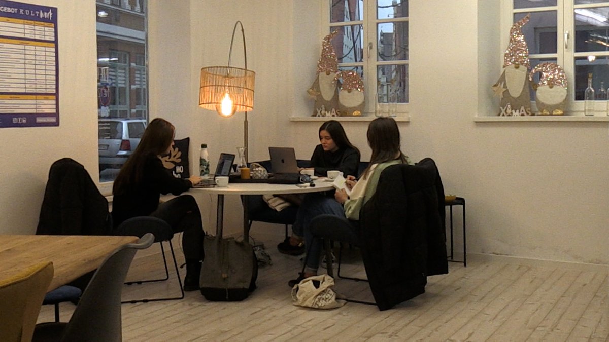 Drei junge Frauen sitzen um einen runden Tisch, hinter dem eine Stehlampe leuchtet