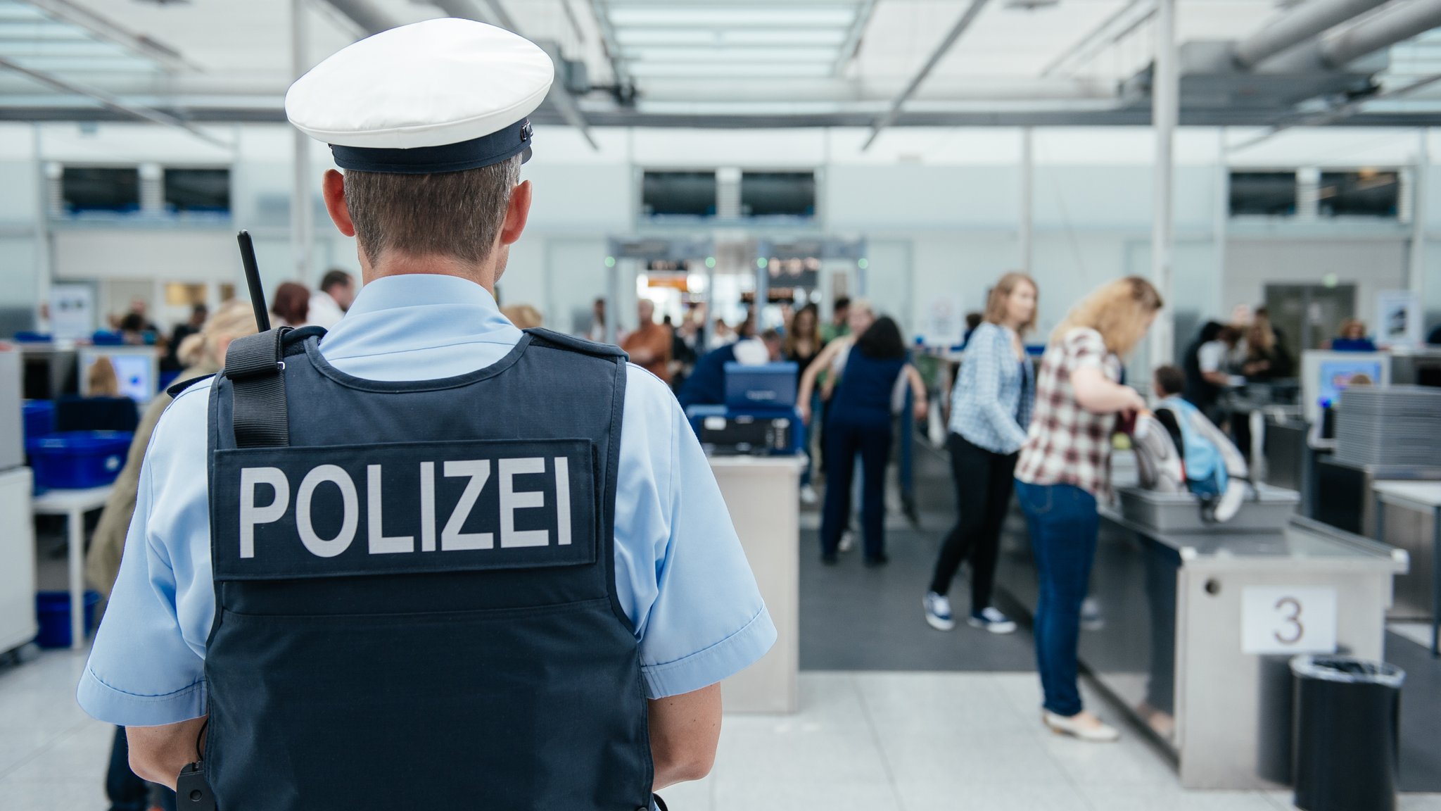 Ein Polizeibeamter überwacht die Sicherheitskontrolle an einem Flughafen (Symbolbild)