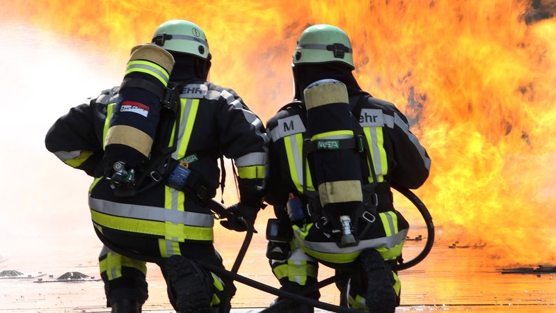 Zwei Feuerwehrleute knien vor einer Flammenwand