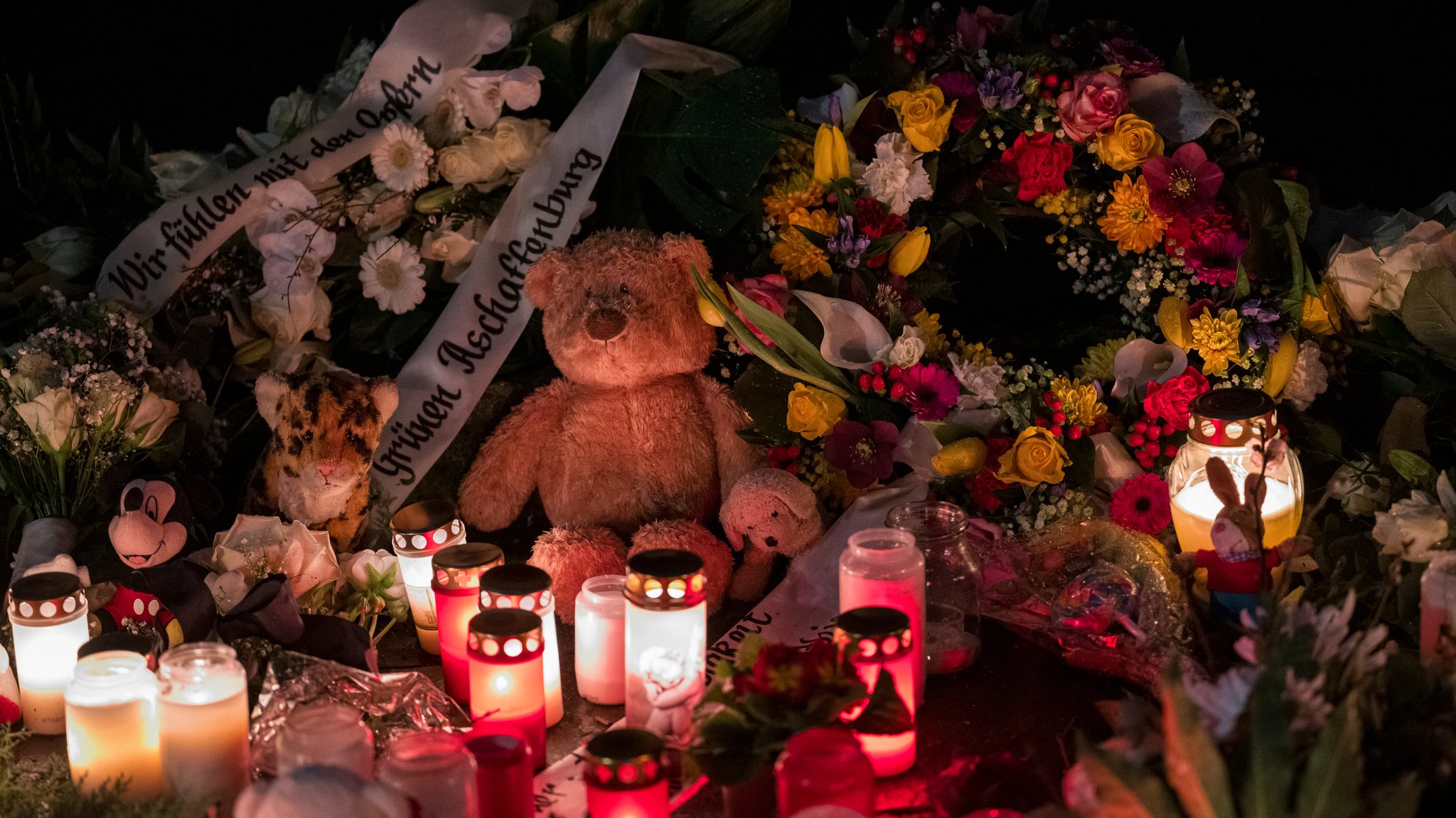 Ein Teddybär liegt neben Blumenkränzen und Kerzen auf dem Boden und erinnert an den tödlichen Messerangriff. 