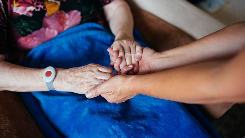 Eine Pflegerin hält einer Seniorin die Hände
