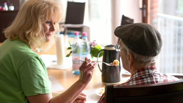 Pflegekraft bei der Arbeit: Die Frau füttert einen älteren Mann.