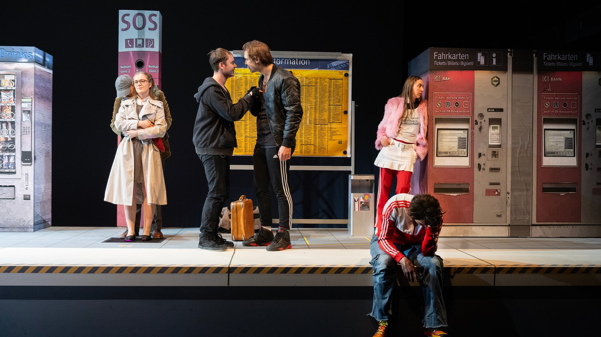 Mitwirkende auf einem Bahnsteig mit Fahrkartenautomat