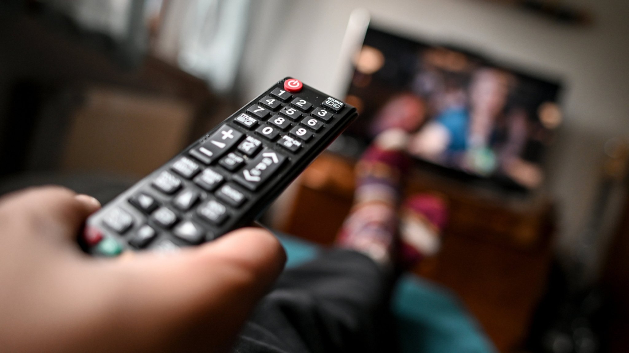 Ein junger Mann sitzt mit einer Fernbedienung vor dem Fernseher.