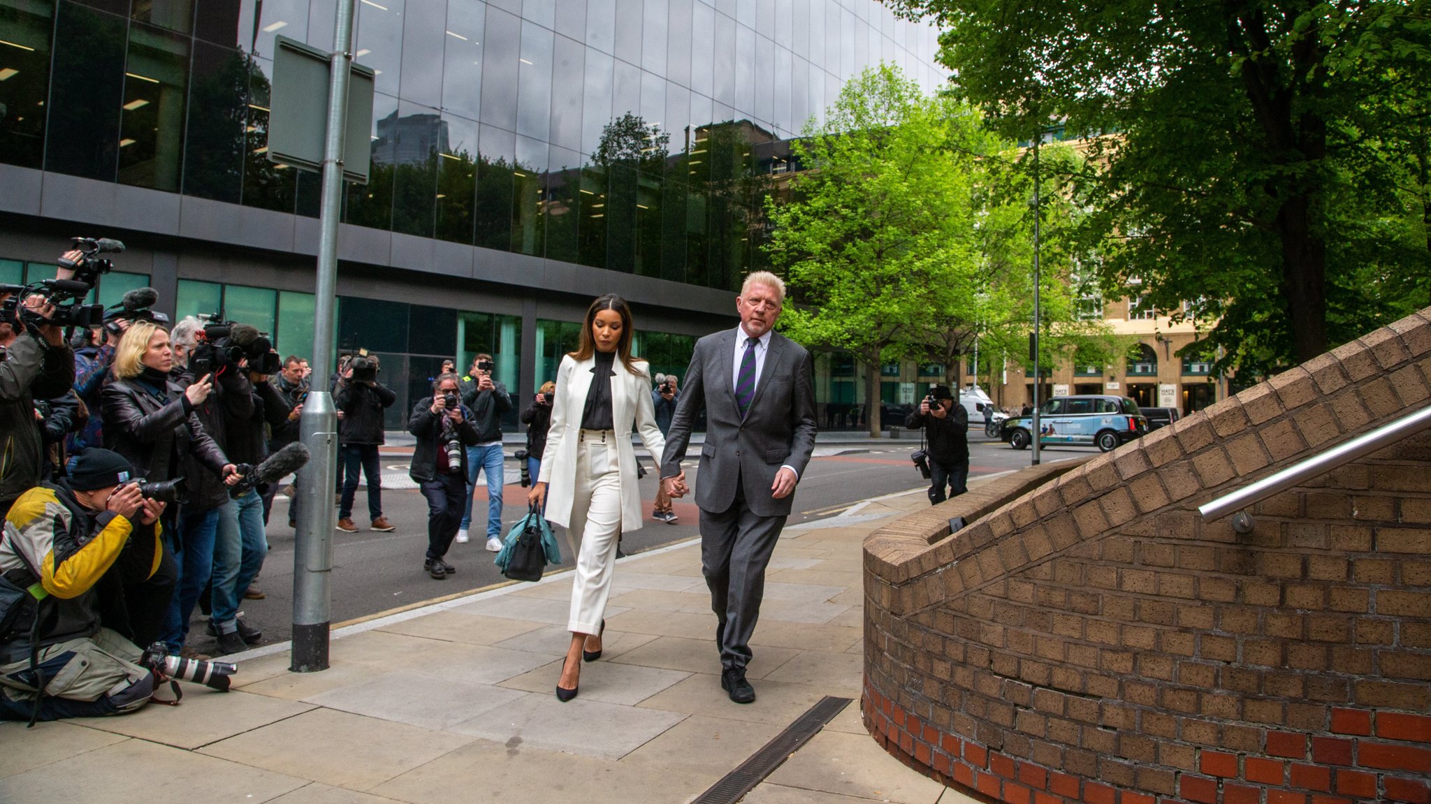 Boris Becker mit seiner Partnerin Lilian De Carvalho vor dem Gericht in London. Im Hintergrund viele Fotografen.