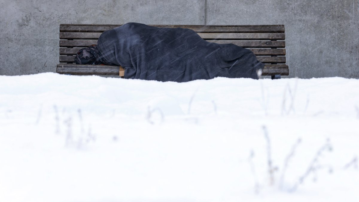 SYMBOLBILD: Eine obdachlose Person liegt bei Kälte und Schnee auf einer Parkbank.