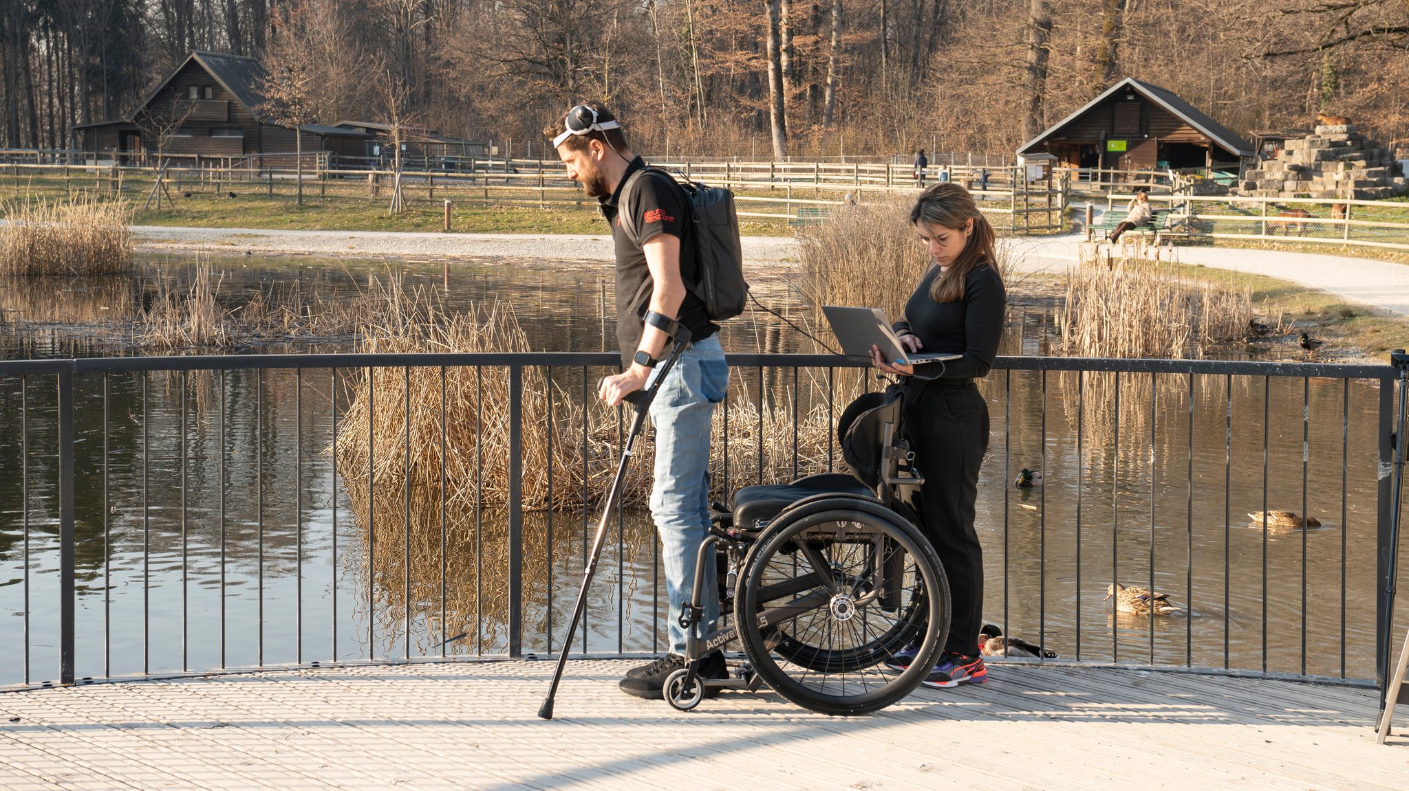 Patient und Wissenschaftlerin mit digitaler Brücke an einem Teich.