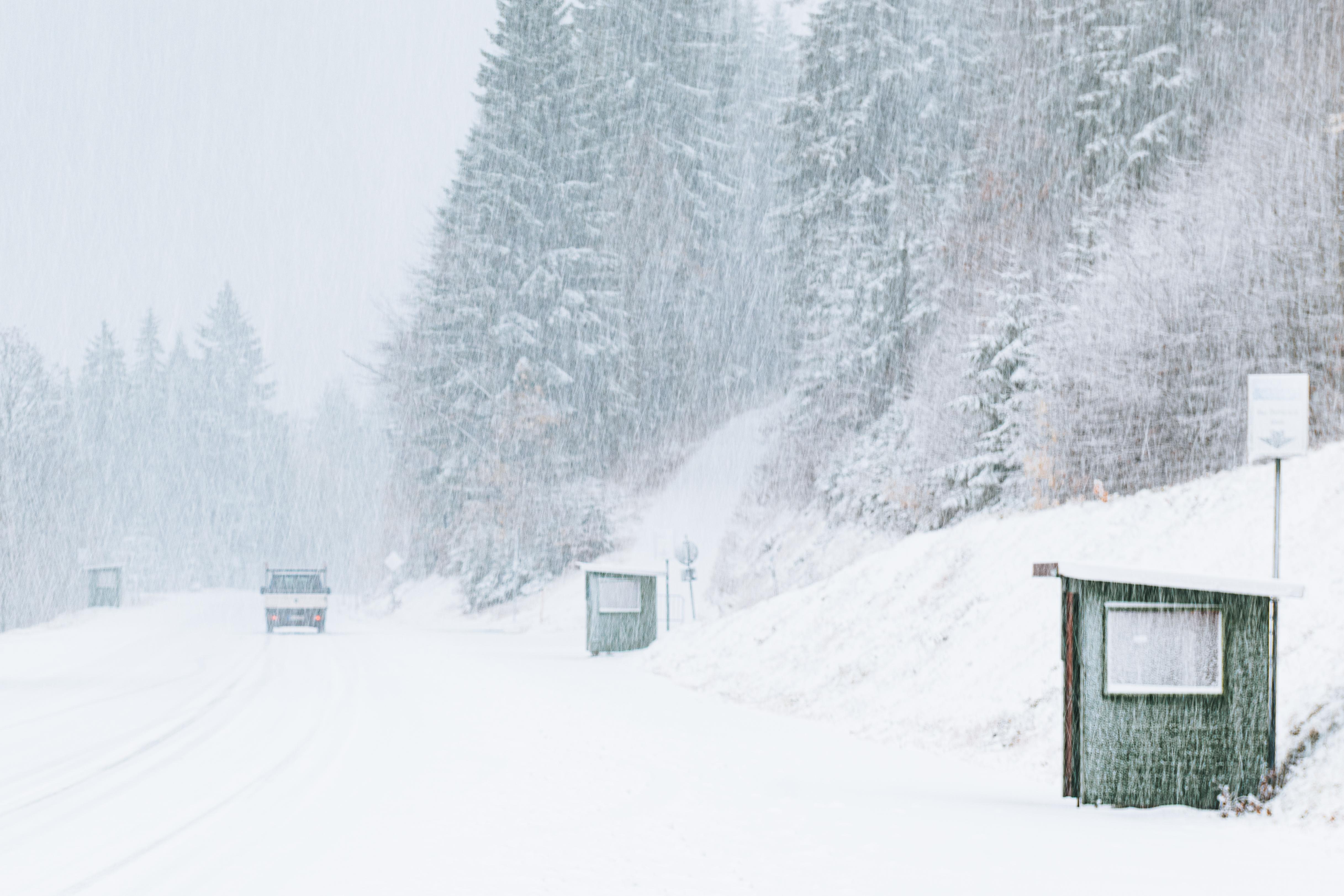 Kleinlaster fährt bei Schneefall auf schneebedeckter Straße durch einen Wald